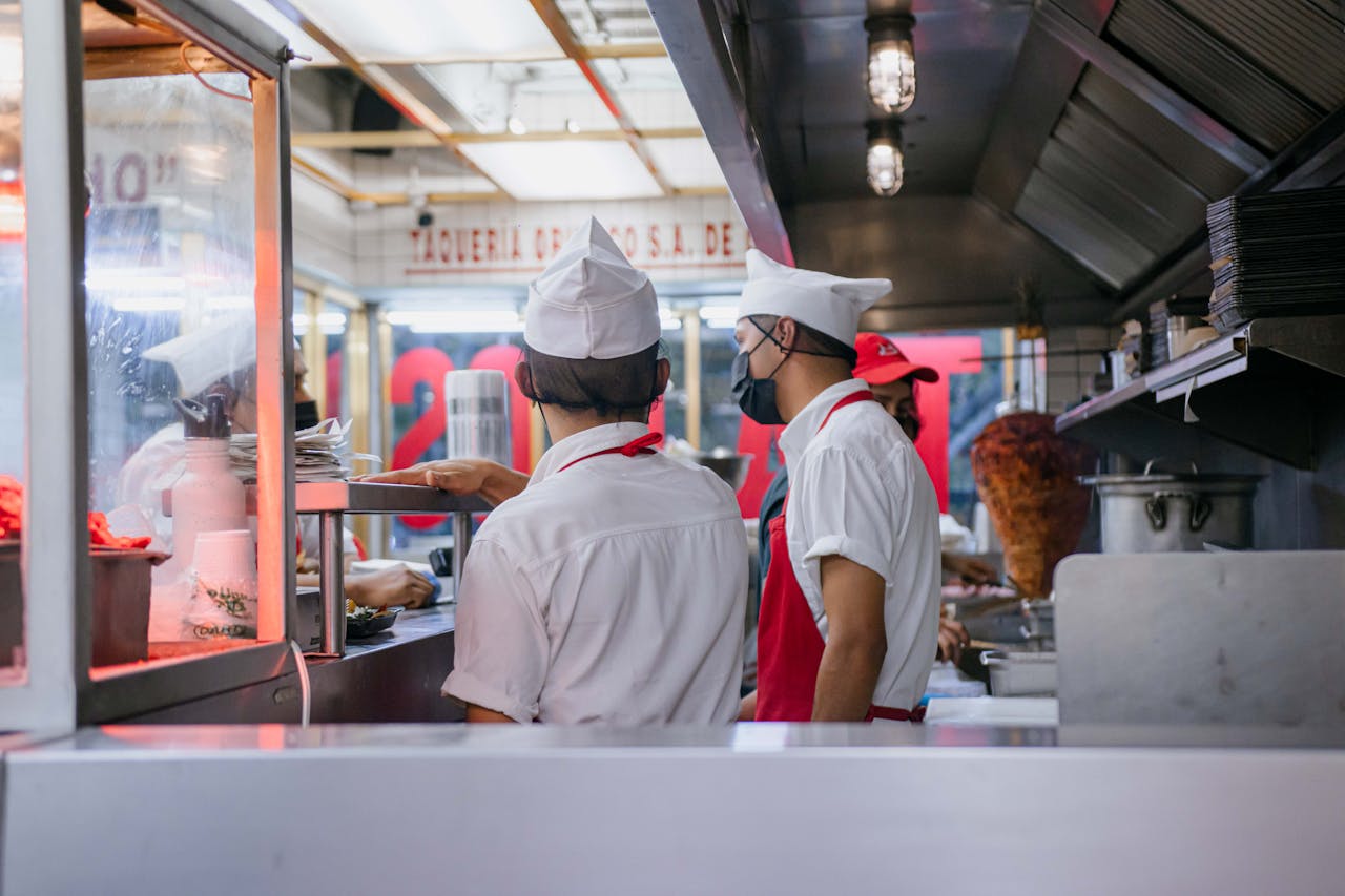 Chefs in uniforms working in an open restaurant kitchen, preparing food orders.